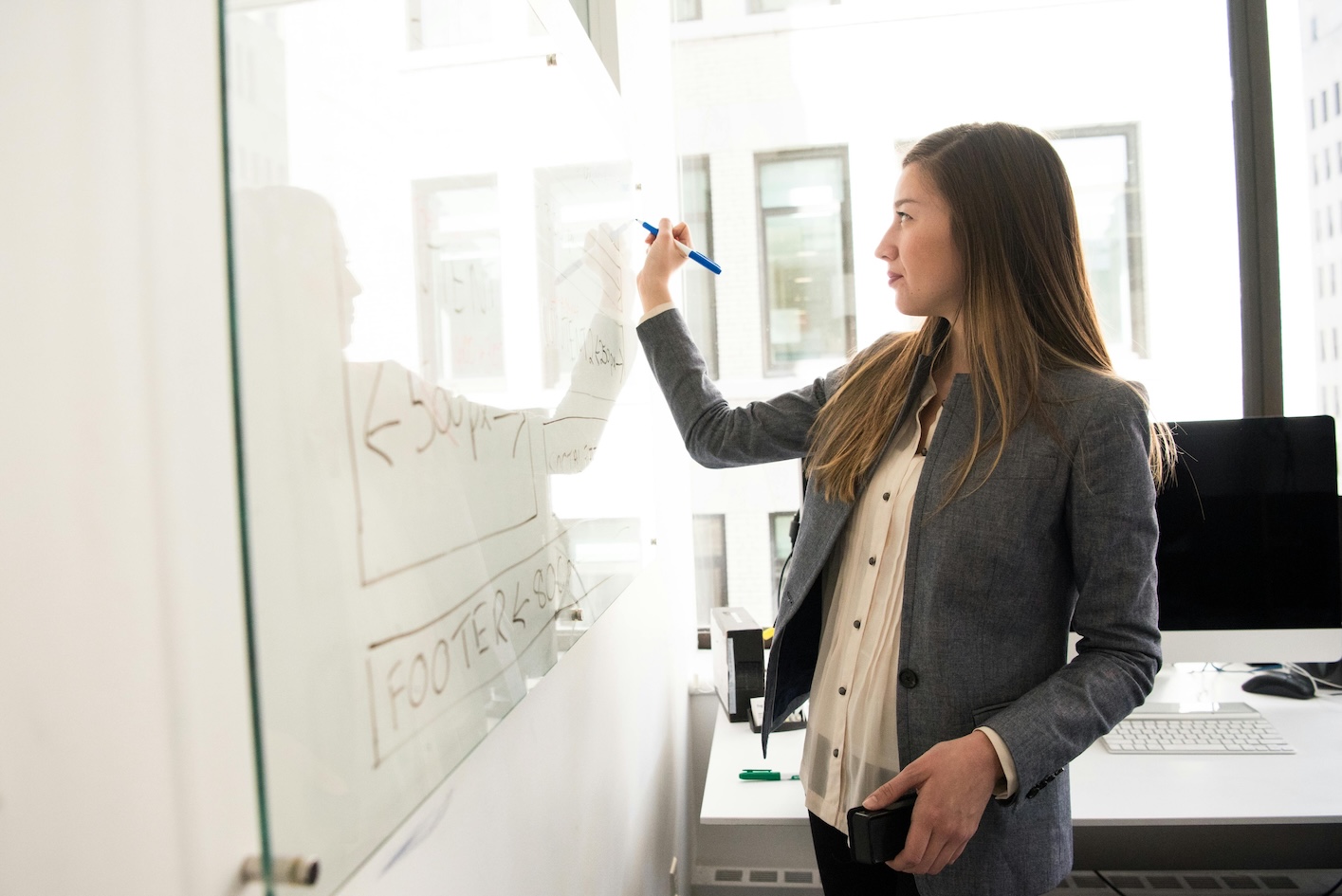 A businesswoman in a suit actively writes on a whiteboard, sharing her insights in a professional setting.