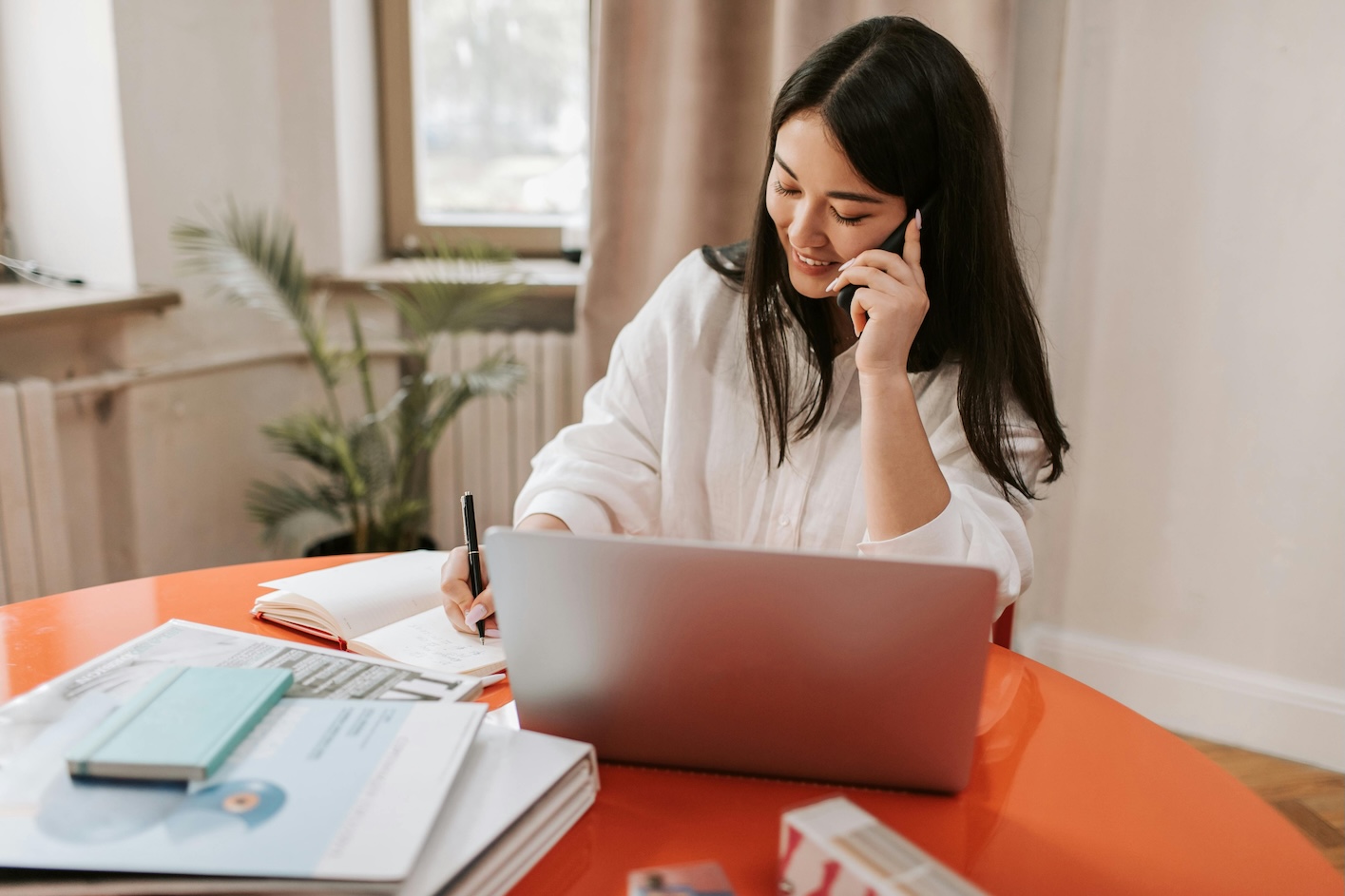 A woman sitting at a table, working on a laptop with a phone beside her.