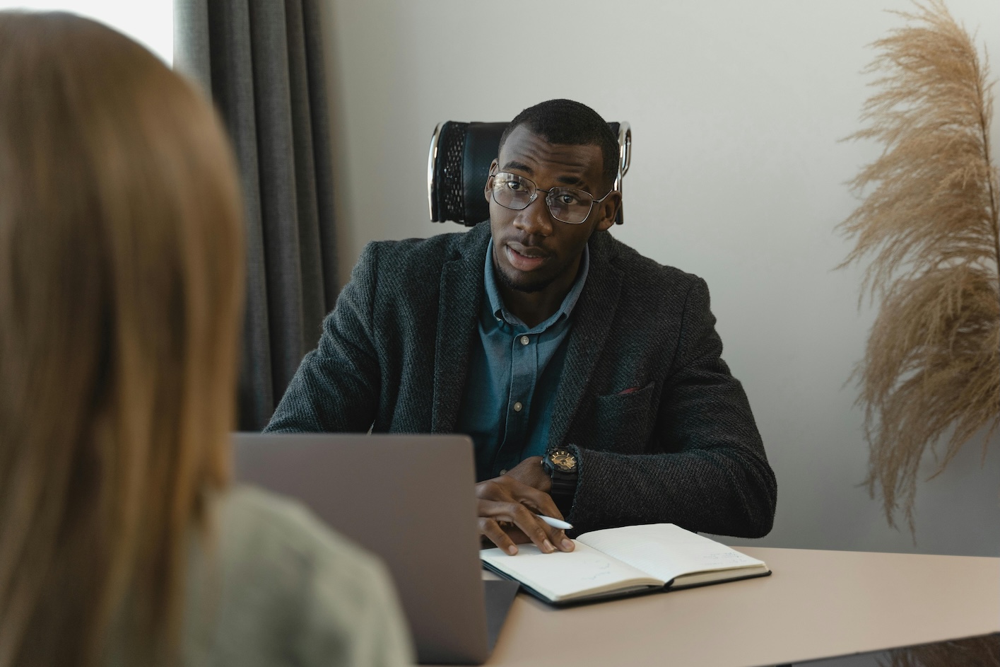 A man in a suit sits at a desk with a woman, both engaged in a discussion.