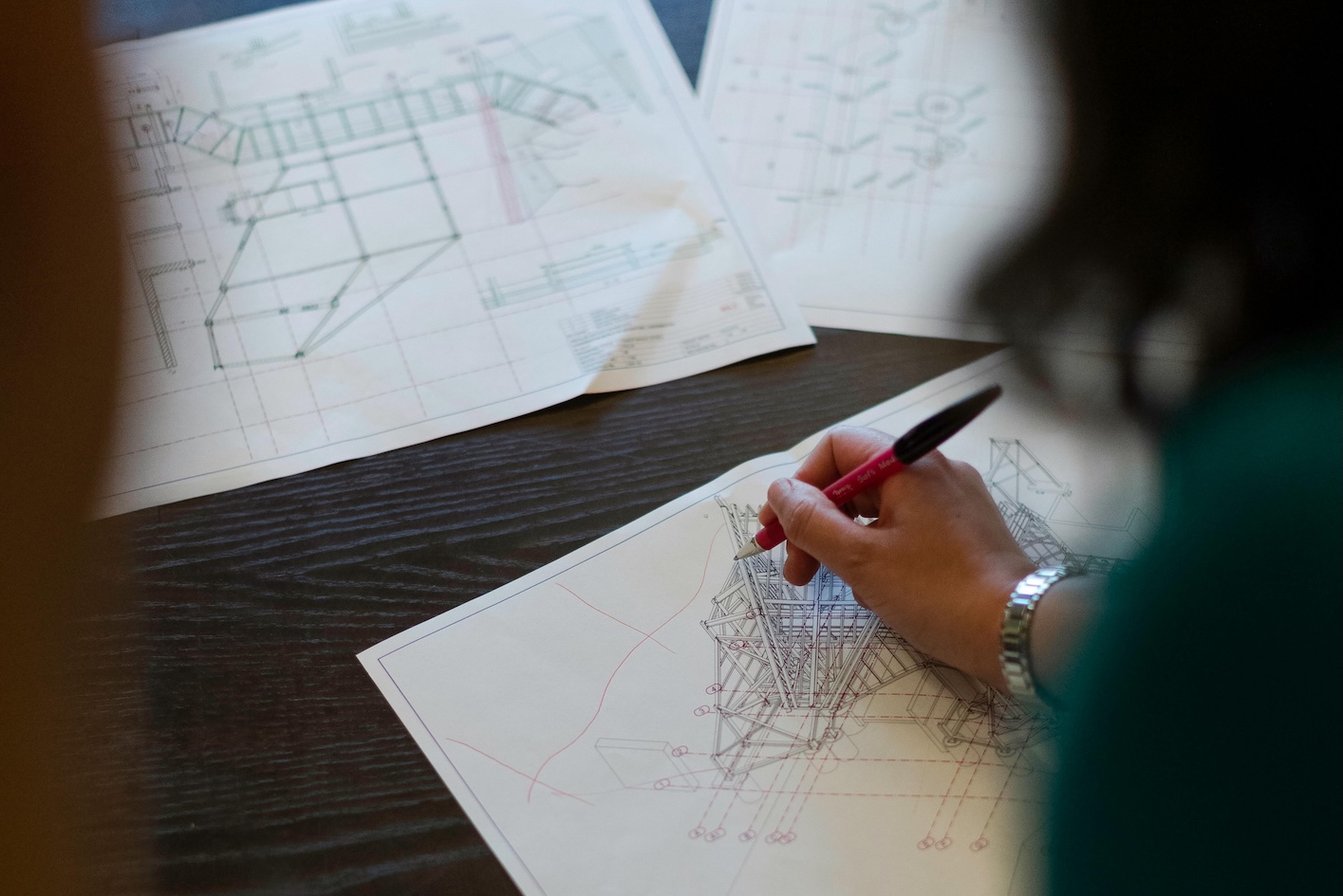 An urban planner sketches architectural drawings on paper using a pen, focused on their work at a desk.