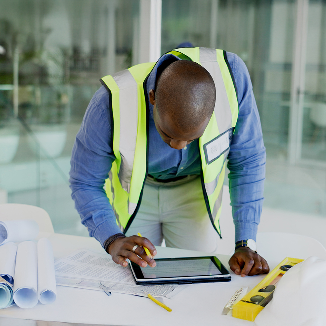 Construction professional reviewing plans and data on a tablet, surrounded by blueprints and tools, illustrating project management and on‑site planning.