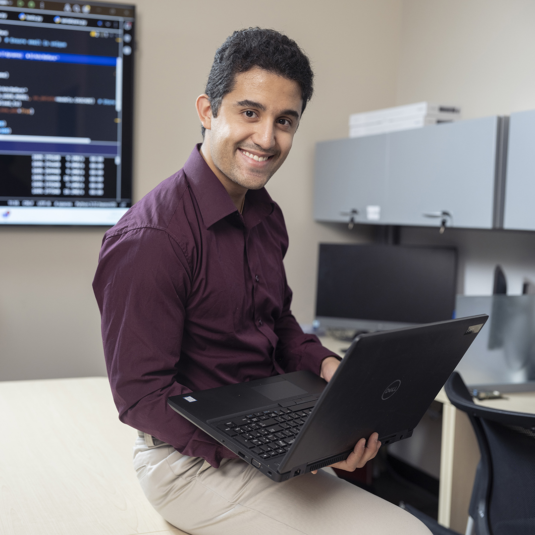 A man sitting on the edge of a desk with a laptop in his hands.