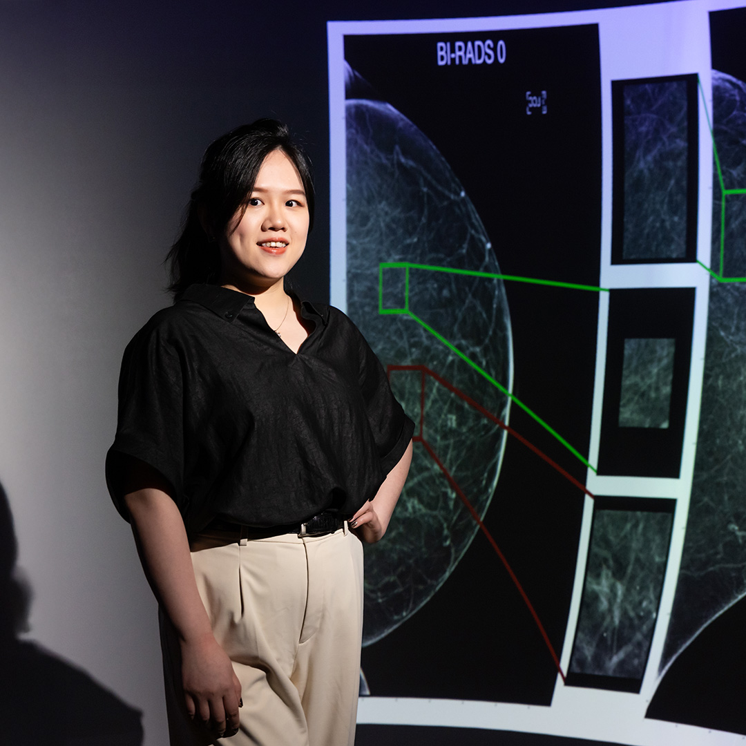A woman is in front of a large display featuring an image focused on breast cancer.