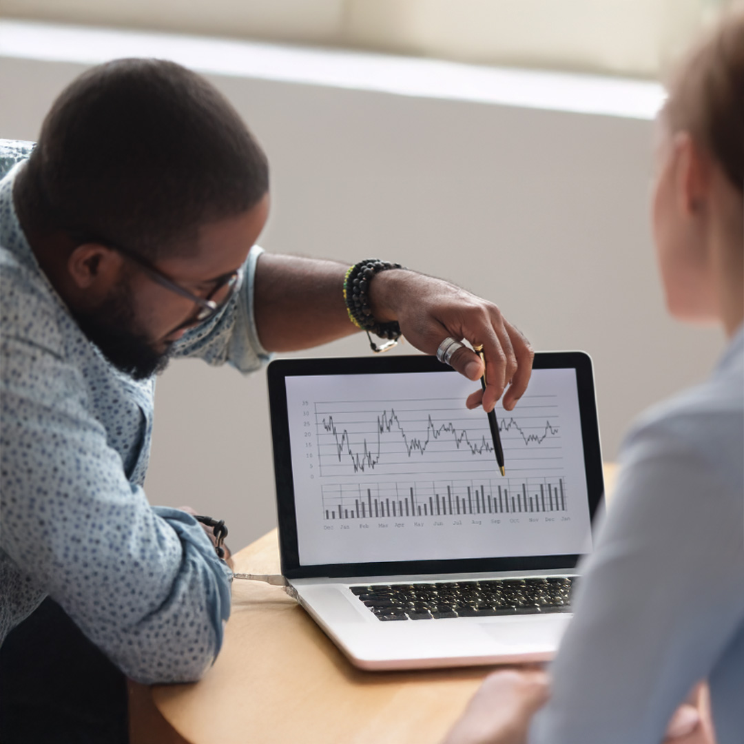 Two people examining a laptop screen displaying a graph, engaged in discussion about the data.