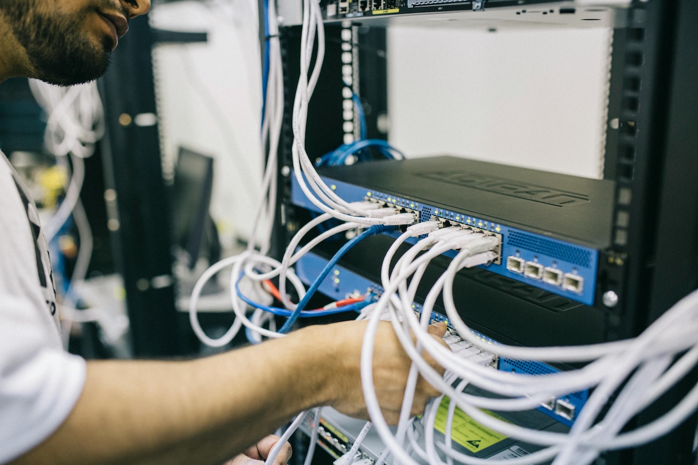 A technician works on a server in a data center, focused on the equipment amidst a backdrop of servers.