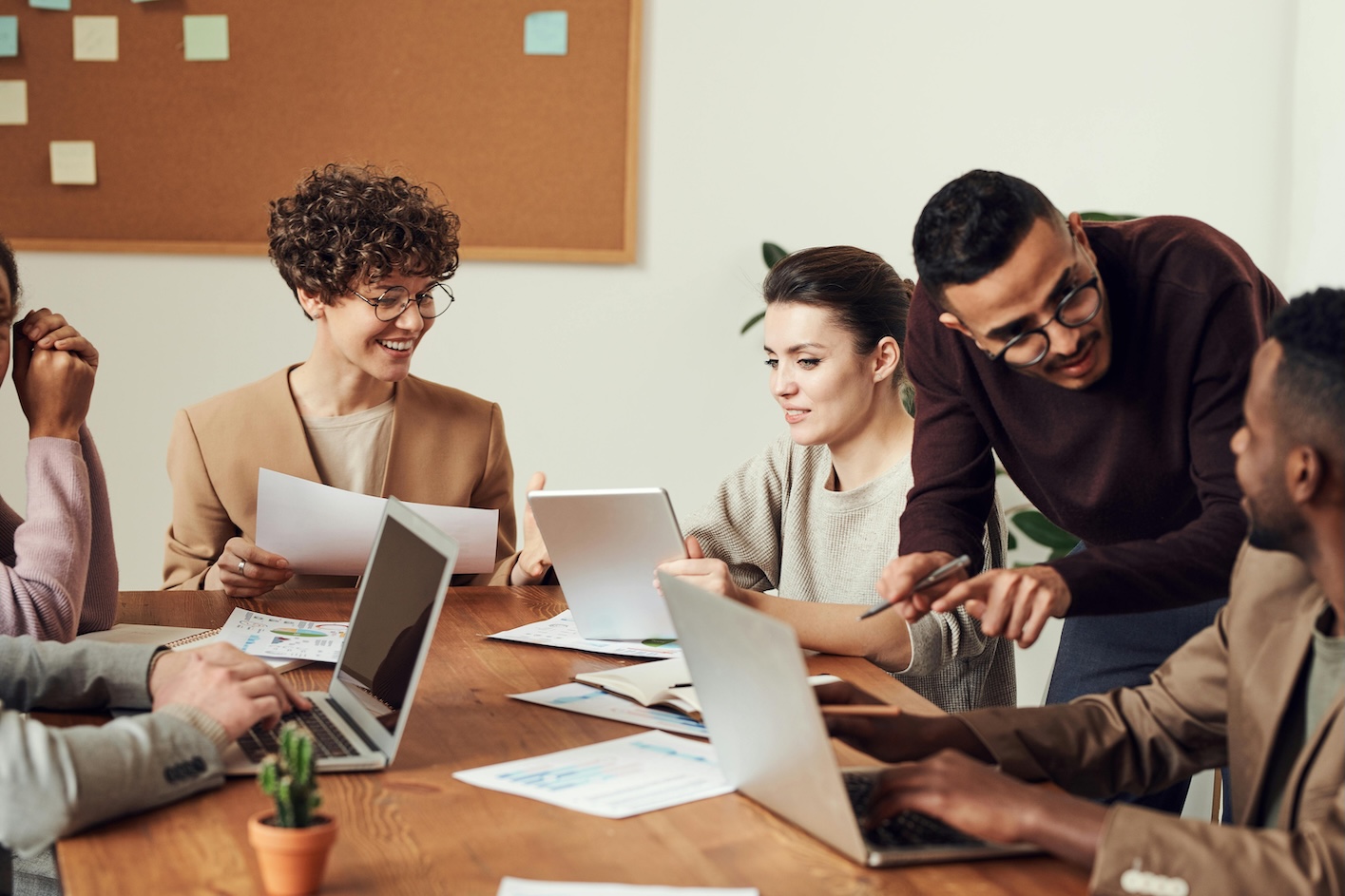 A team of people gathered around a table, each with a laptop, actively participating in a group discussion.