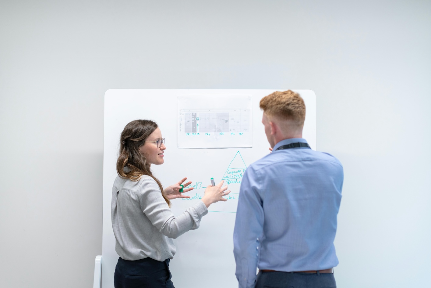 Two people standing in front of a whiteboard, discussing ideas and taking notes during a collaborative meeting.