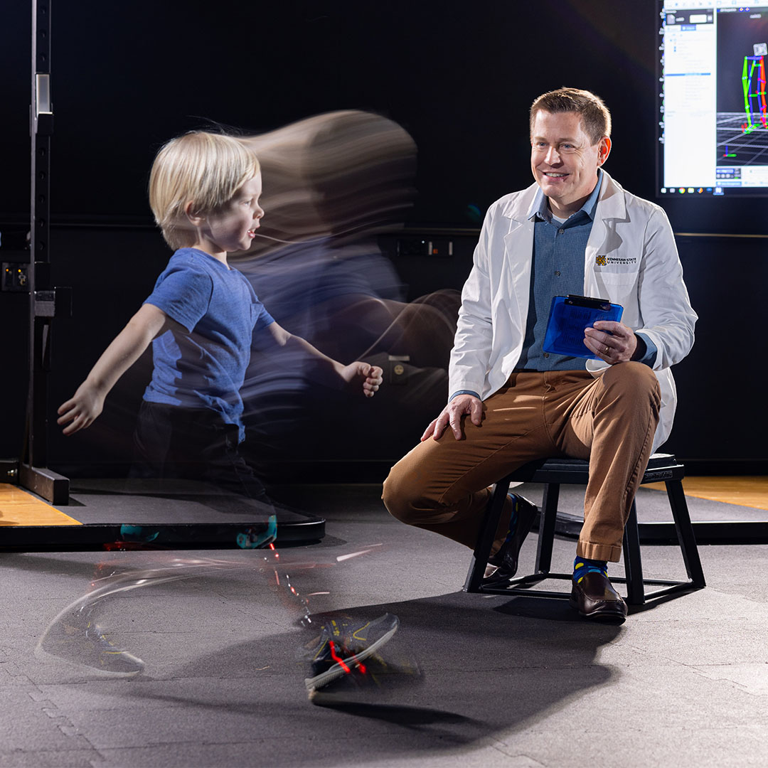 Graduate exercise science student performing VO₂ max testing on a stationary bike using a metabolic cart, while another student records data in a physiology lab equipped with multiple cycle ergometers.