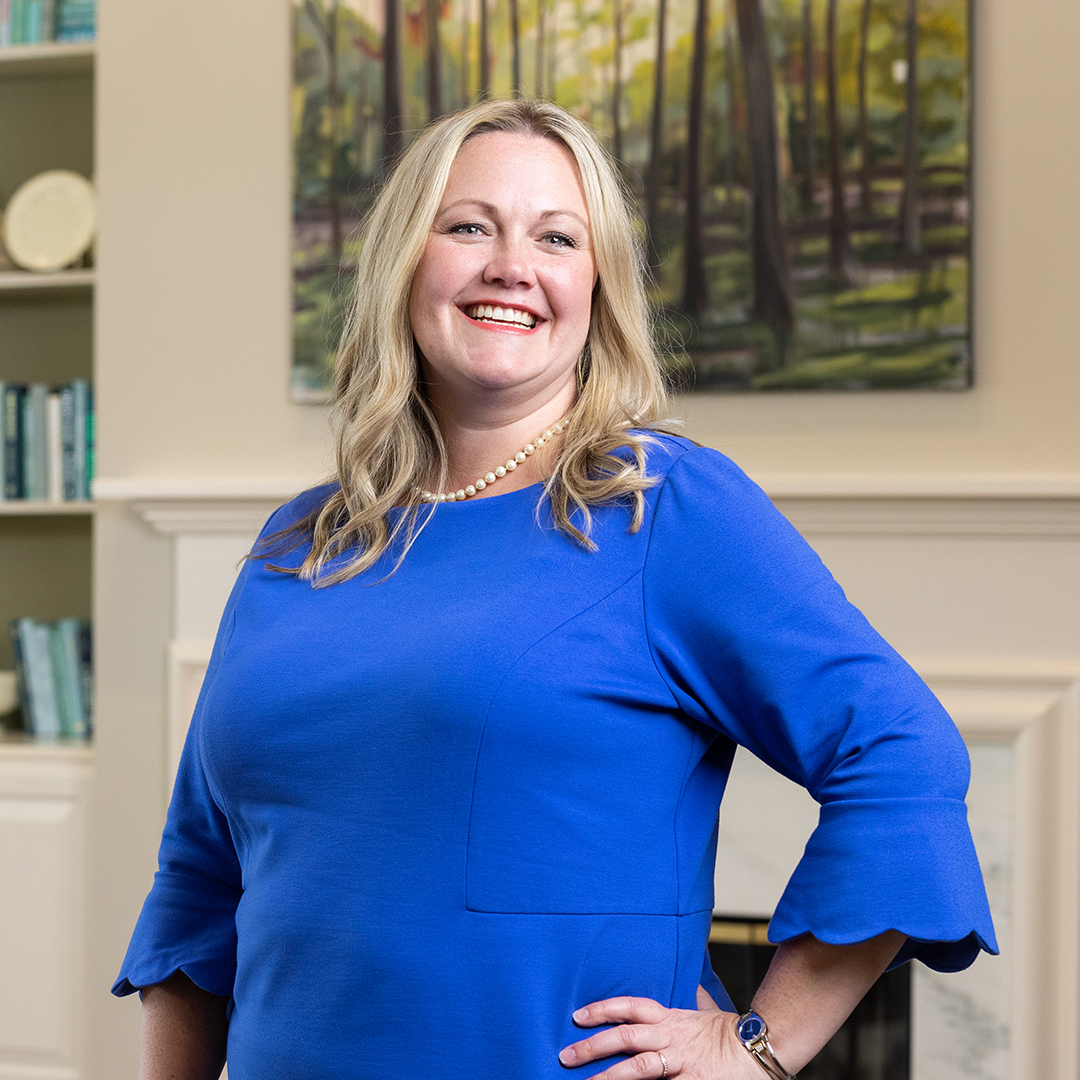 A woman in a blue dress stands in front of a fireplace.