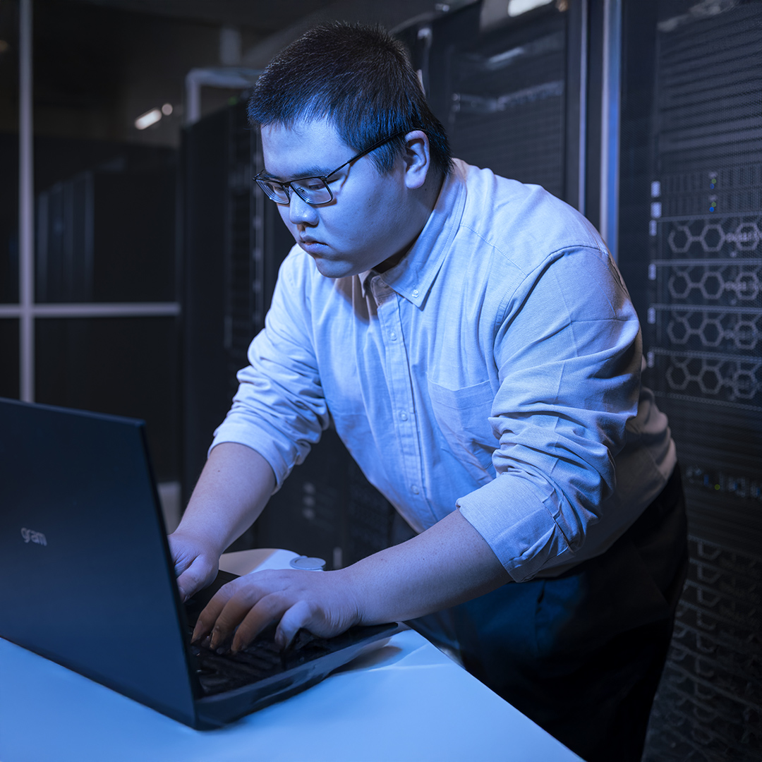 Man in a dark server room is typing on a computer laptop.