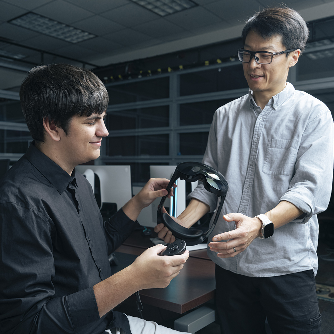 Two individuals engage in a discussion about virtual reality equipment in a tech environment.