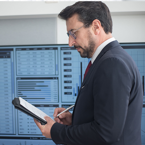 man in glasses and suit looking at paper in front of computer system