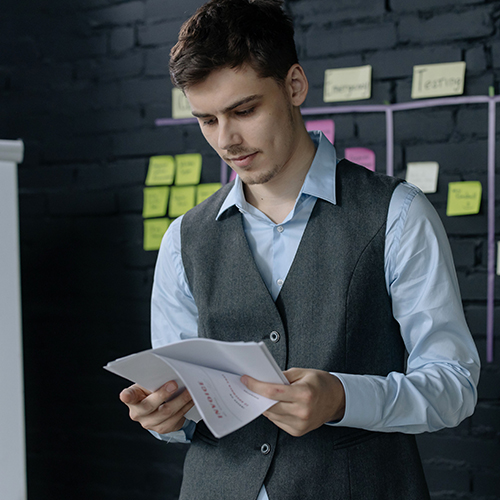 man in suit holding papers in office in front of sticky notes board