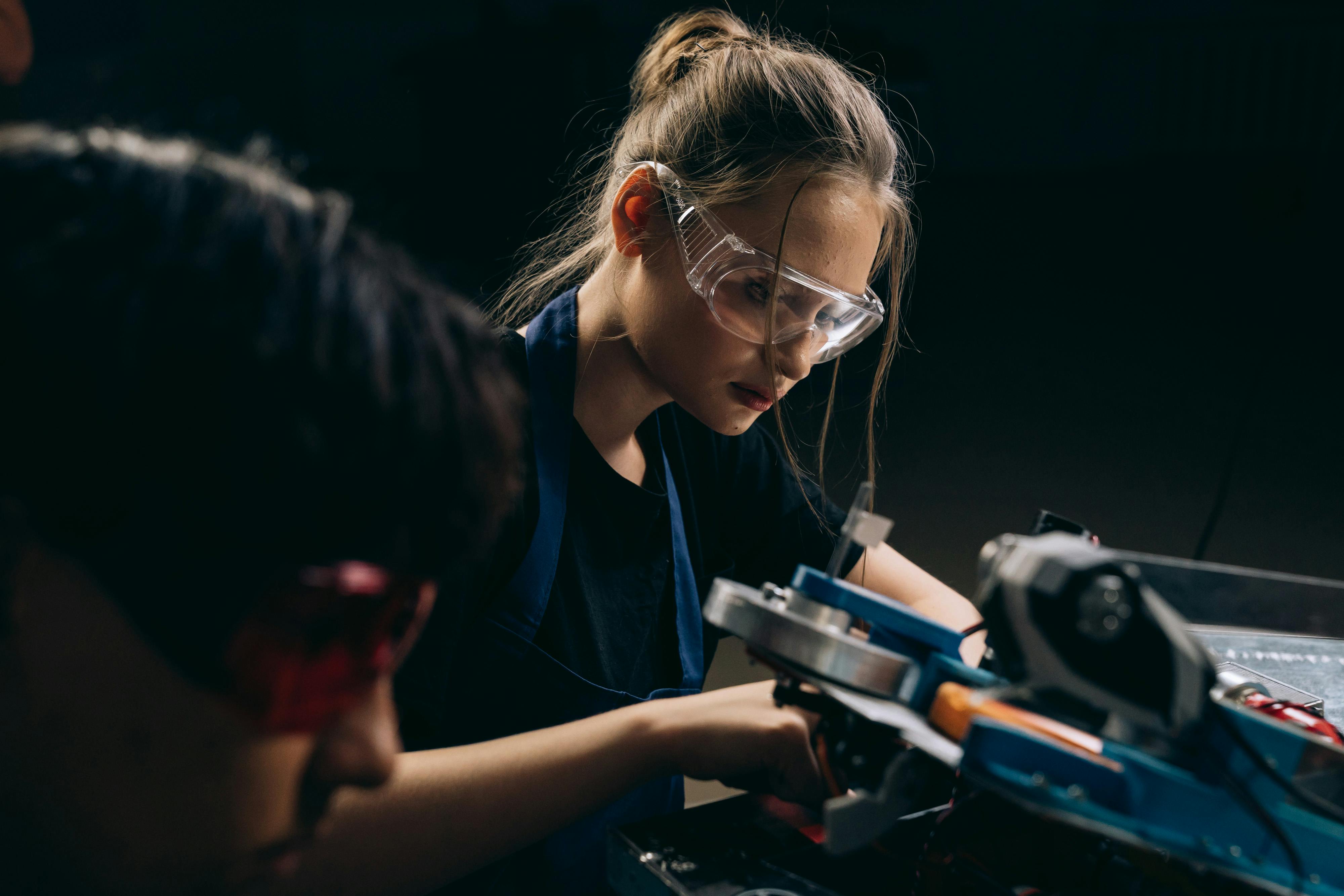 Two young people collaboratively operating a machine in a workshop setting, focused on their task.