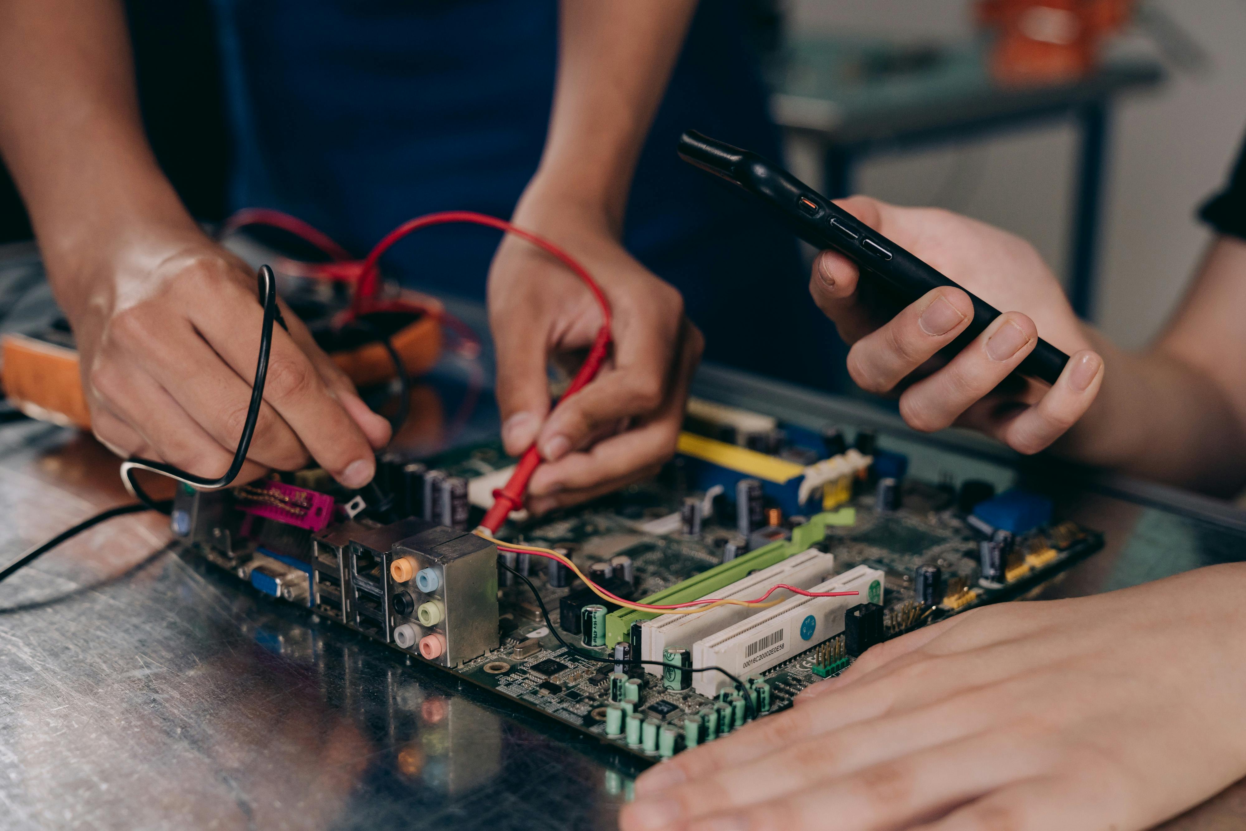 Two people engaged in work on a computer motherboard, examining and connecting various electronic parts.
