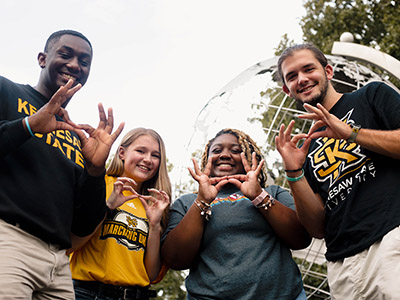 group of ksu students smiling holding owl hand gesture