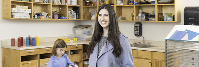Female teacher smiling as young student works behind her