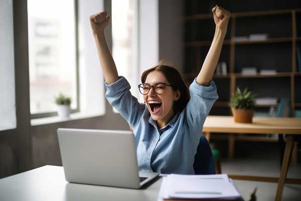 girl with hands in the air and big smile with laptop on desk in front of her.