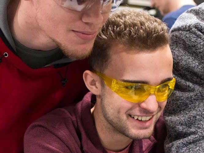 Two men with safety goggles looking down and focusing on a project