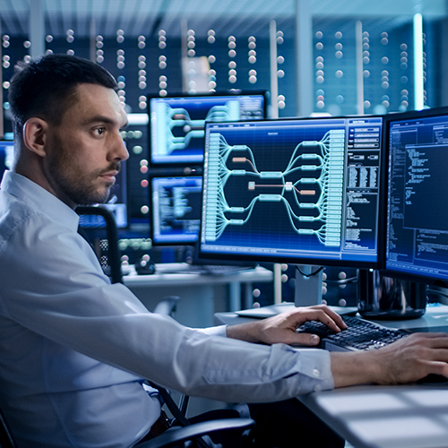 man sitting at computer station wiht 4 monitors with data