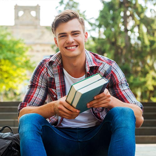Graduate student sitting on campus holding their book.