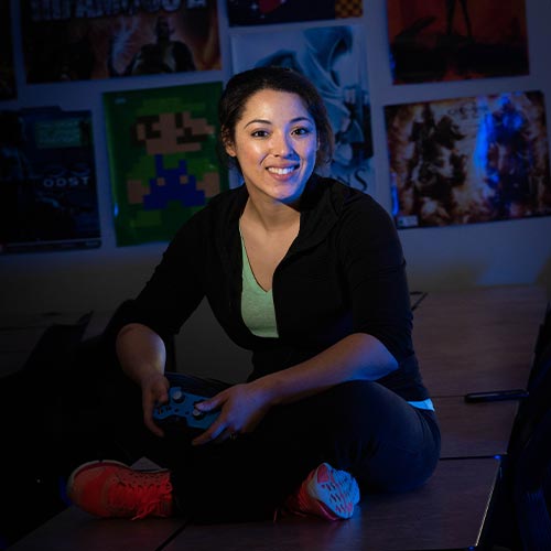 KSUstudent sitting on a table holding a gaming controller smiling for picture.