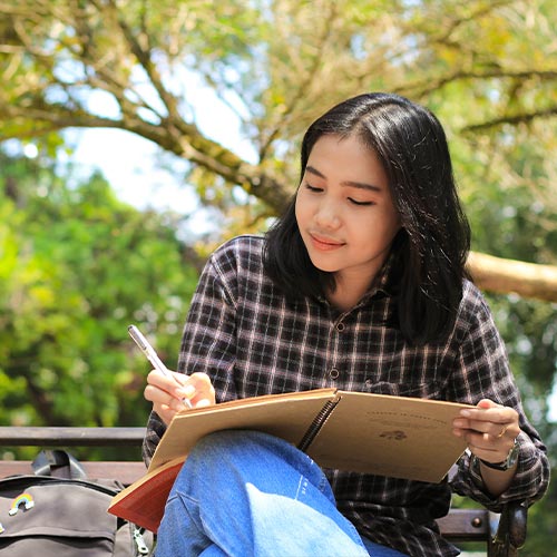 KSU student sitting on campus taking notes.