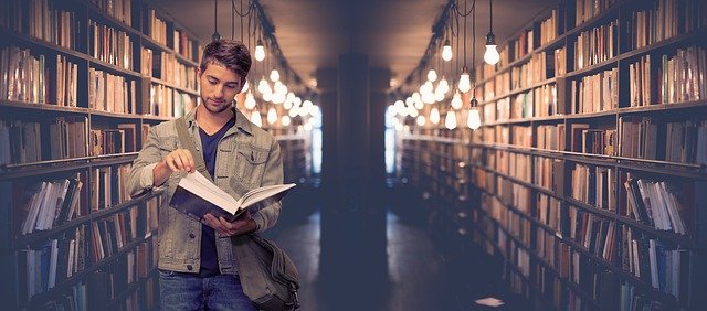 student in a large library standing looking at a book.