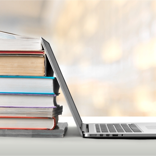 an open laptop leaning on a stack of textbooks
