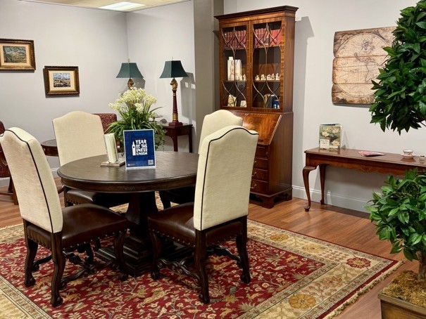 a photo of the reading room with a table, chairs , bookshelves and plants.