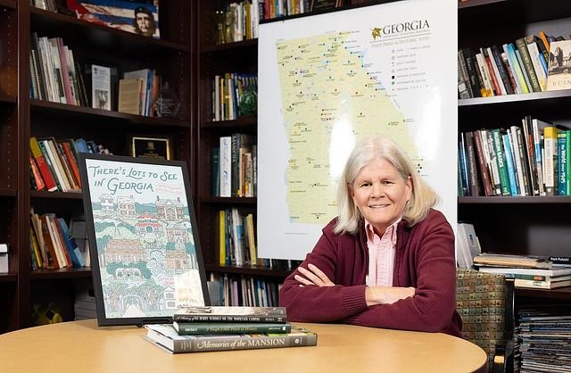 Dr. Jennifer Dickey sitting at a table with a stack of books in front of her and a map of Georgia behind her.