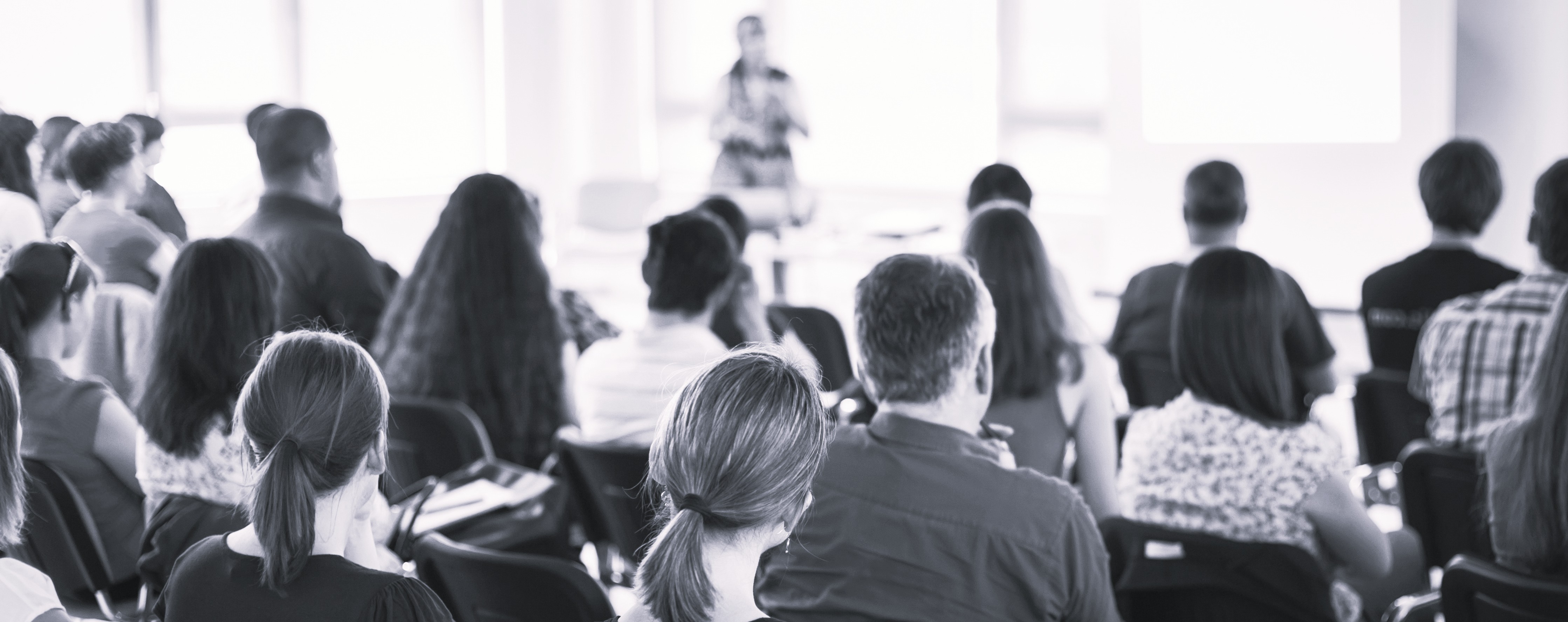 black and white photo showing an audience listening to a presenter