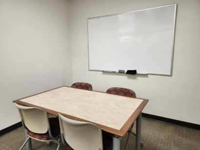 A study room with a table with four chairs and a whiteboard on the wall in the background