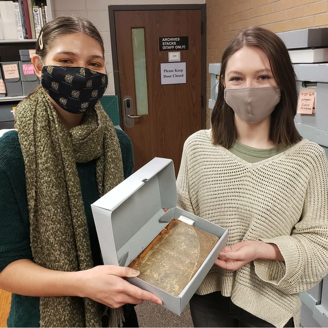 Archives interns Morgan Bendzinski (left) and Abigail Mead holding a phase box they created to preserve a rare book.