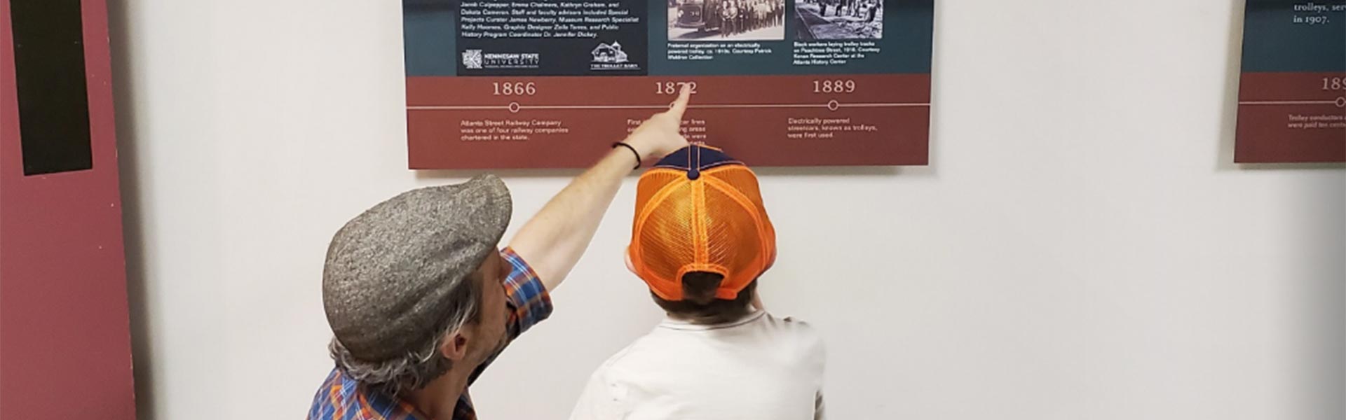 Father and son looking at a history plaque on the wall.