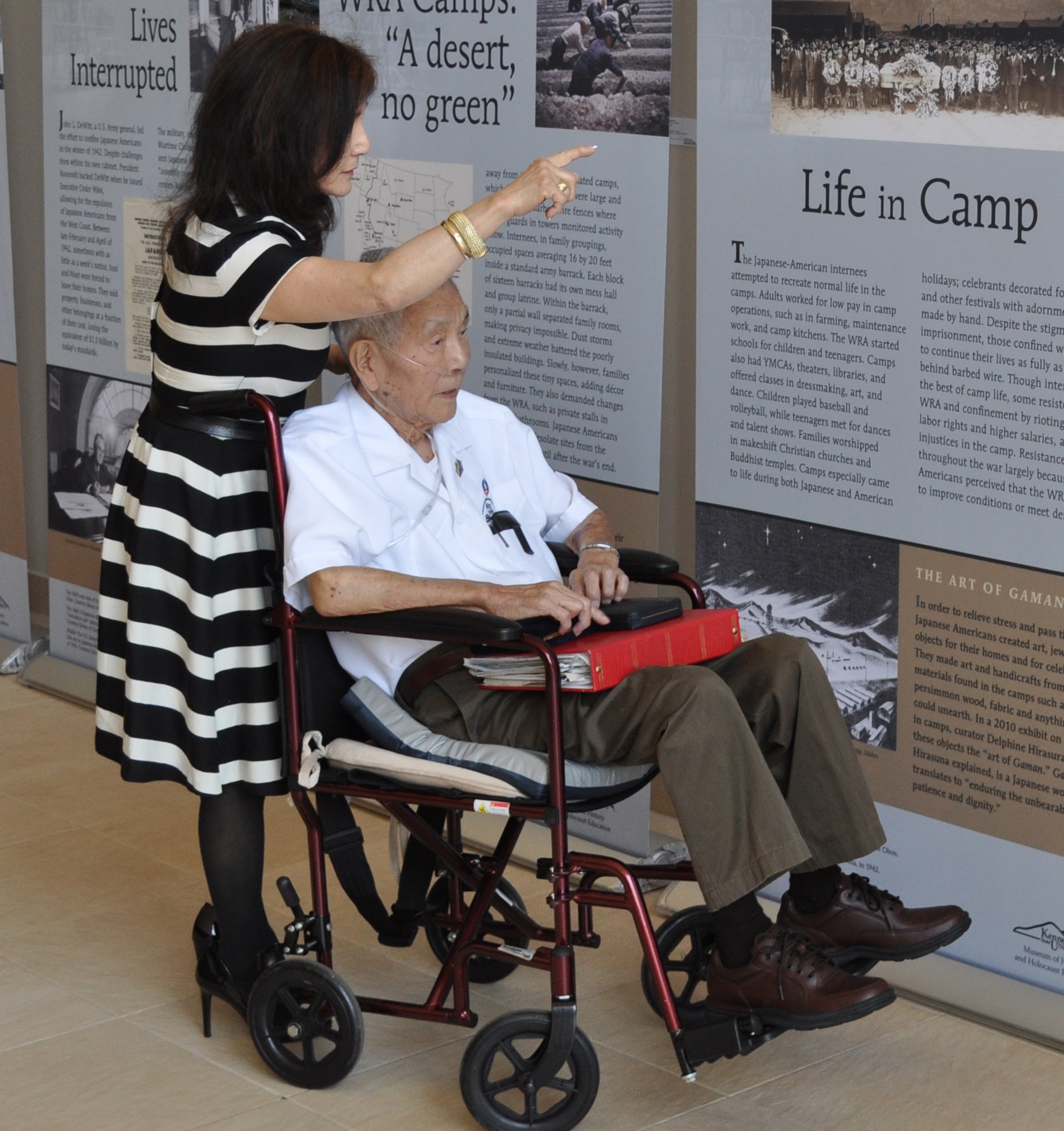 A woman guides a man in a wheelchair through an exhibit