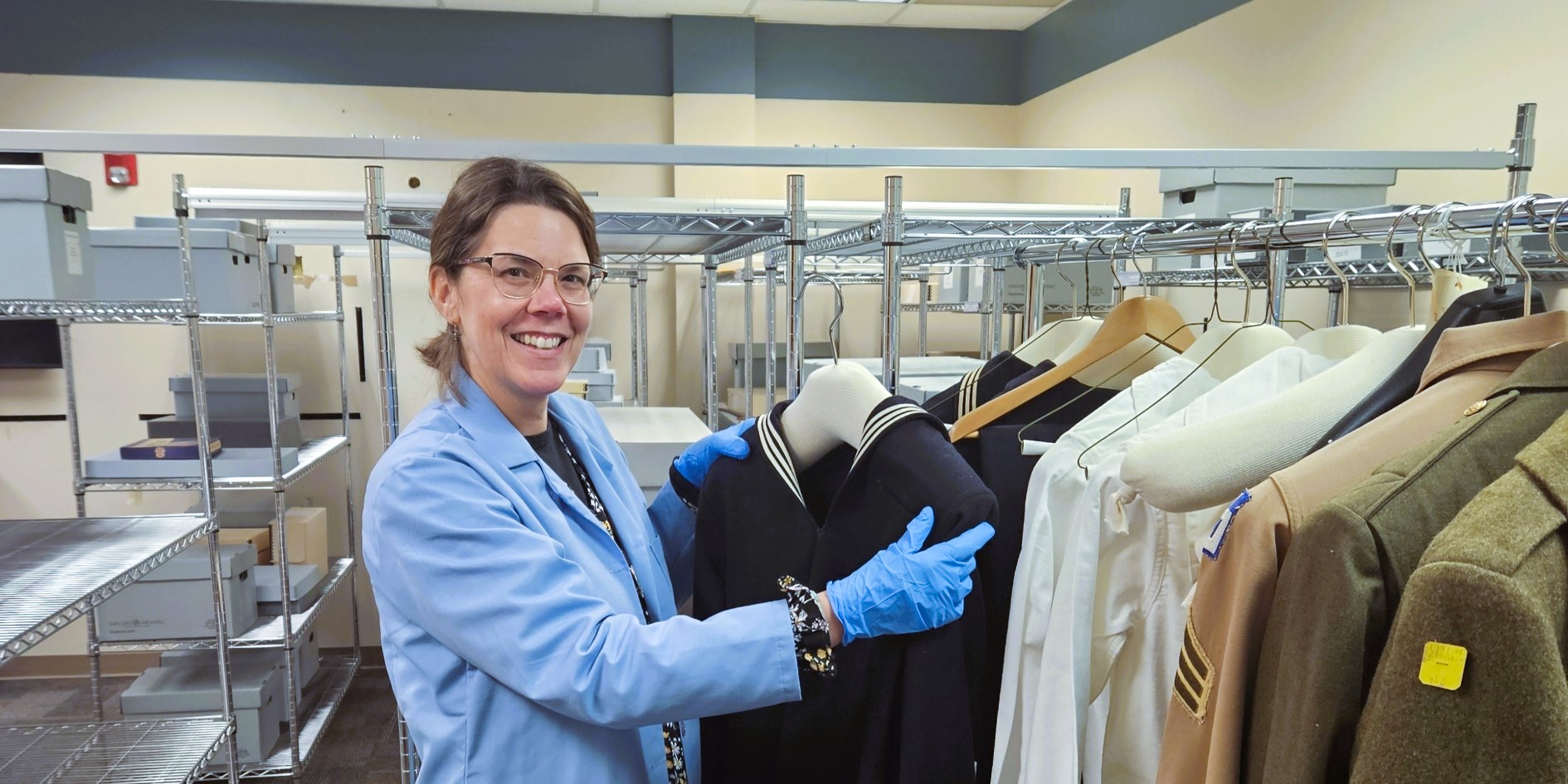 A woman wearing protective gloves and gown showing a navy blue seaman's uniform top.