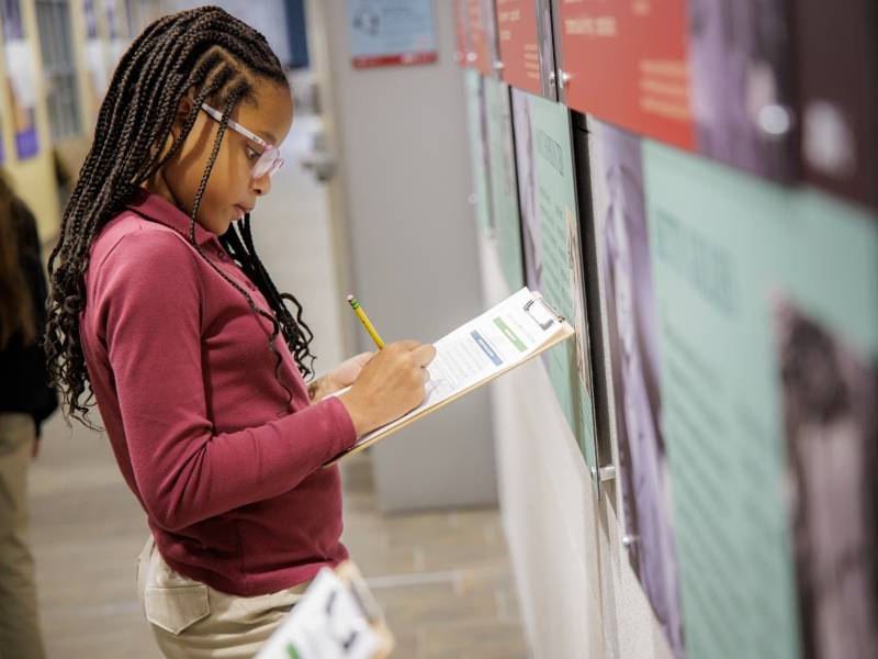 A young girl with a clipboard completing an assignment at the museum