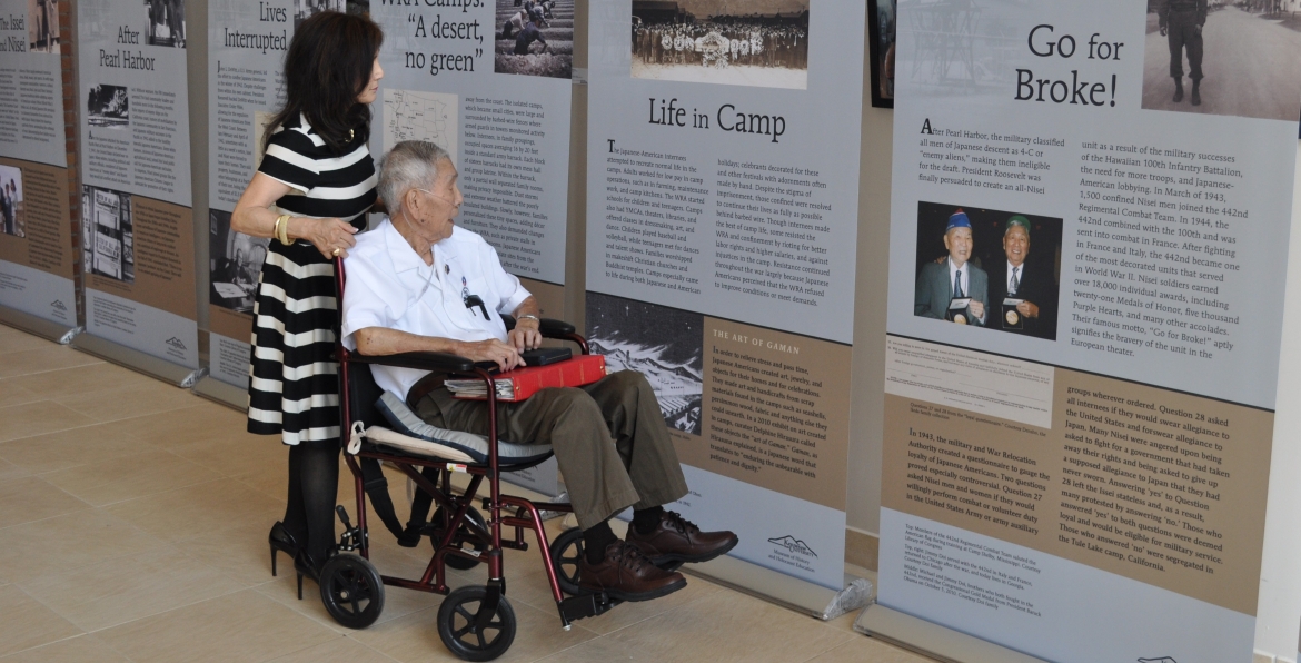 A woman pushing a man in a wheelchair while they look at a museum exhibition