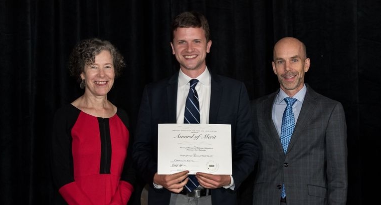 Three people stand together holding up an award