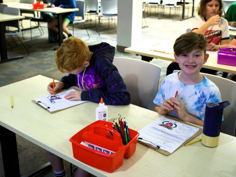 Two young boys are sitting at a table working on a coloring activity during one of the MHHE home school day events
