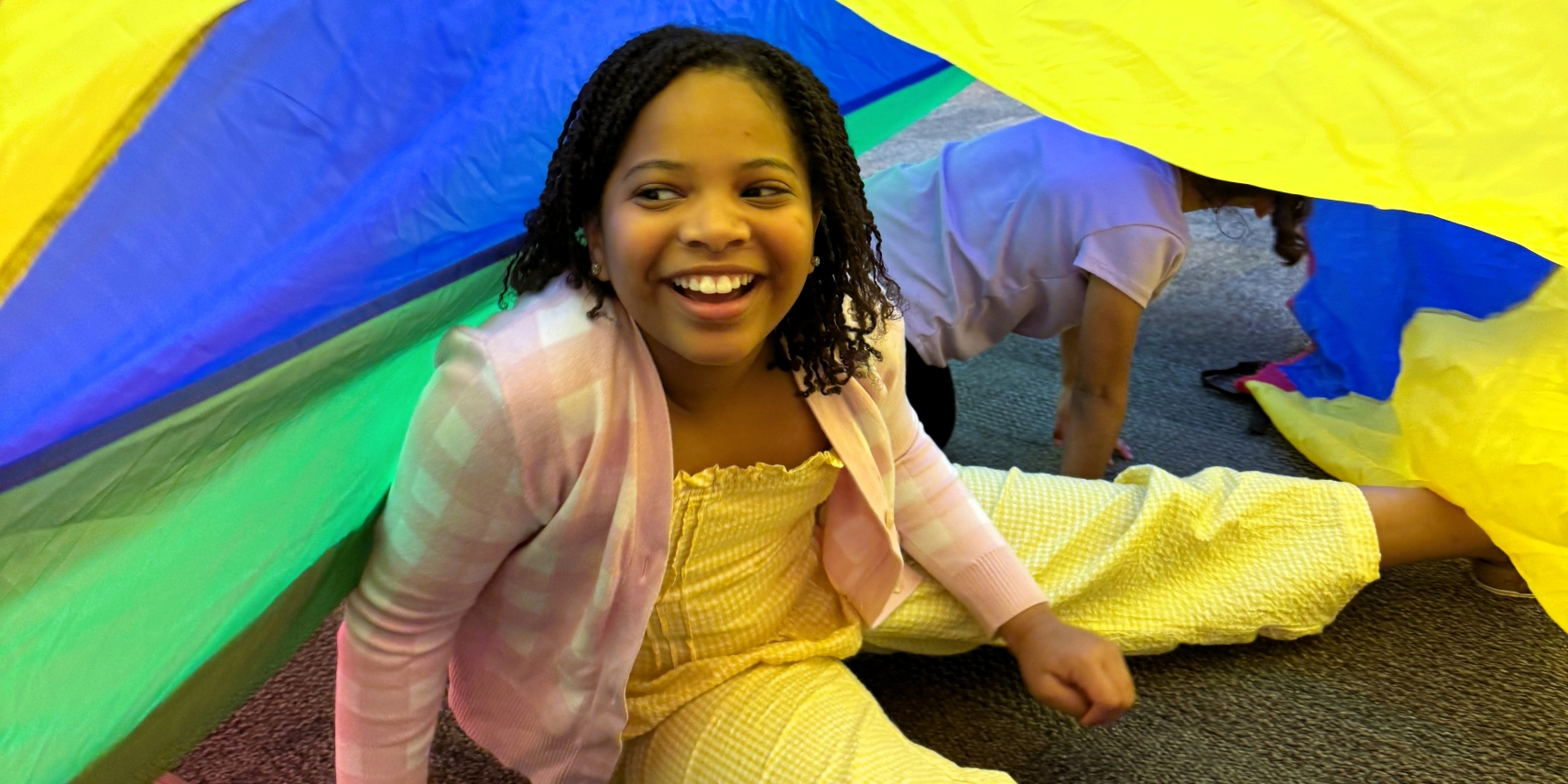 a joyfully smiling little girl sitting on the floor under colorful fabric