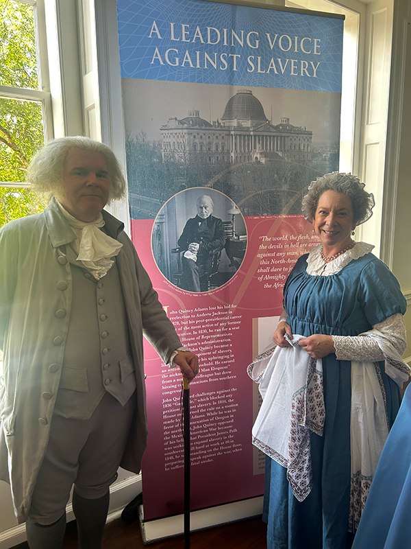 A man and woman dressed in historical costumes standing in front of an exhibit panel