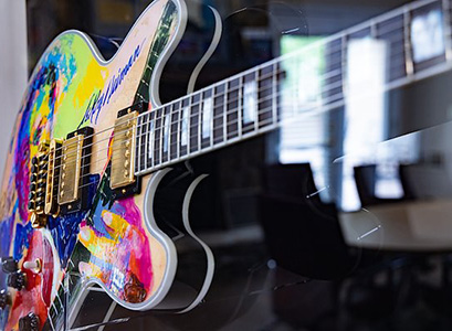 The image showcases a vibrant, custom-painted electric guitar featuring a colorful abstract design.