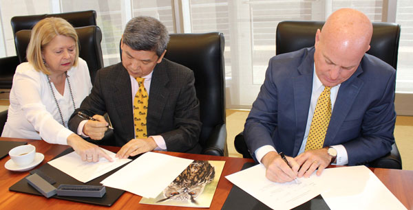 Three people sitting at a table signing a paper.