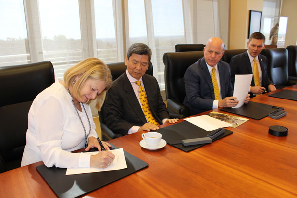 Karen Takada signs the document at a table with three people watching.