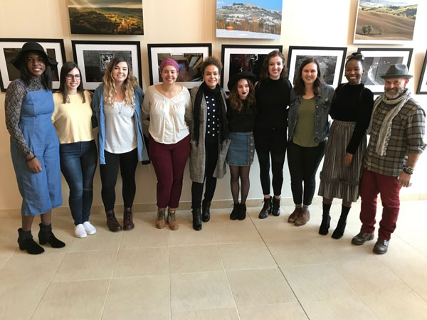 A group stands and smiles in front of a wall of photos.