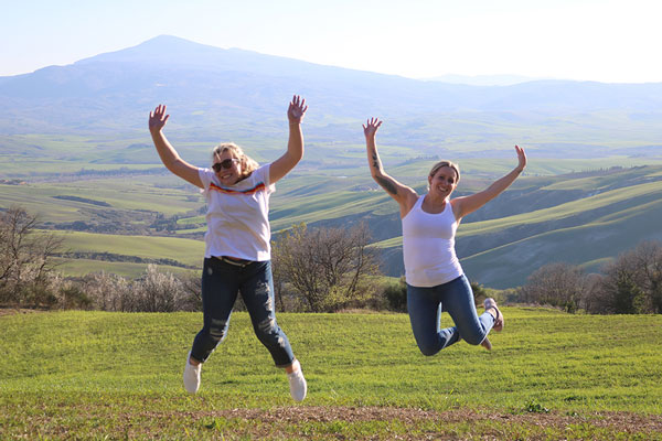 Two girls in white tshirts jumping in the air with tuscany in the background
