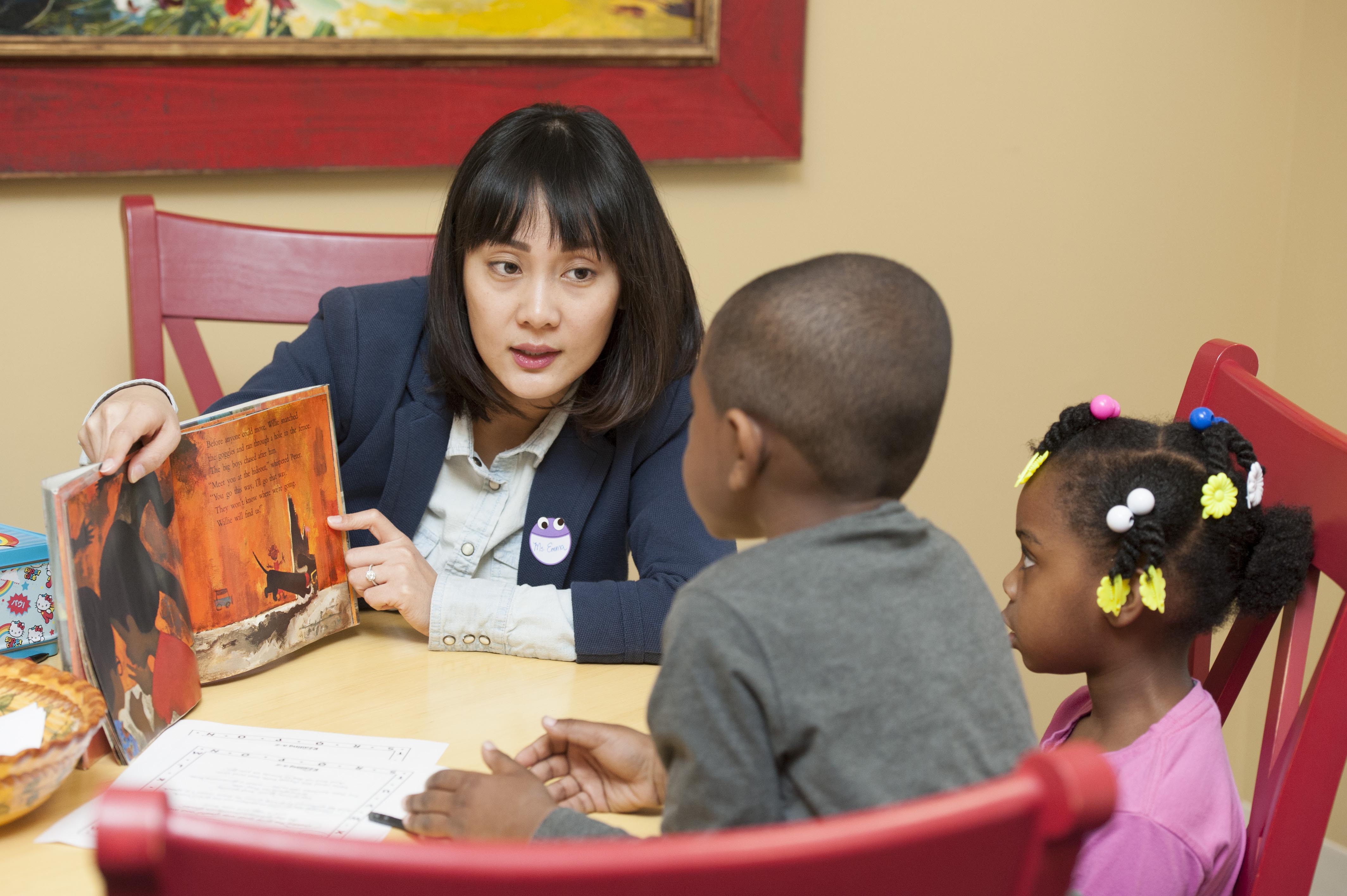 female teacher reading colorful book as she smiles to students with arms raised