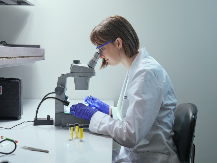 A person in a white lab coat uses a microscope in a laboratory